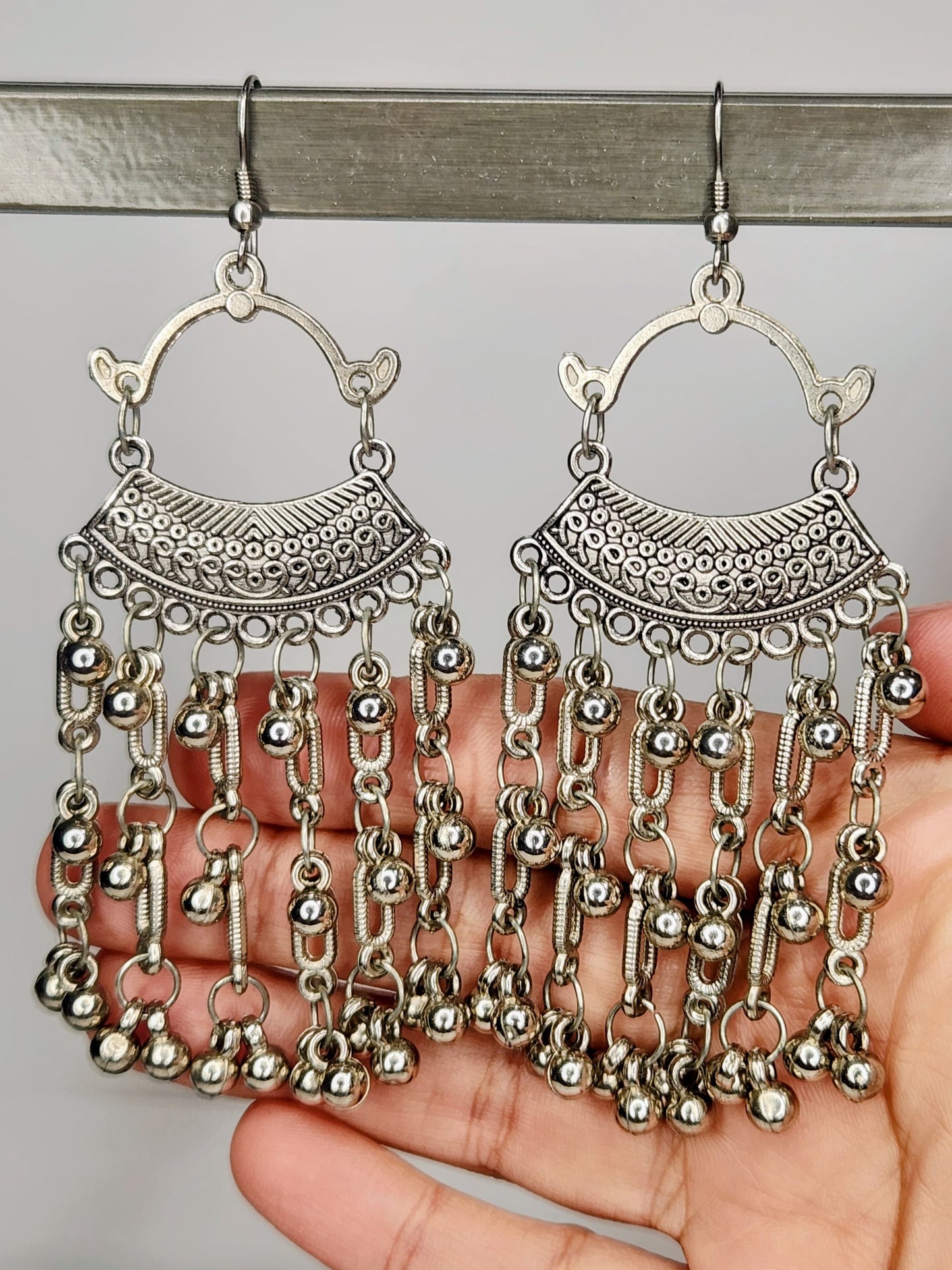 Silver chain earrings held by a hand against a neutral background