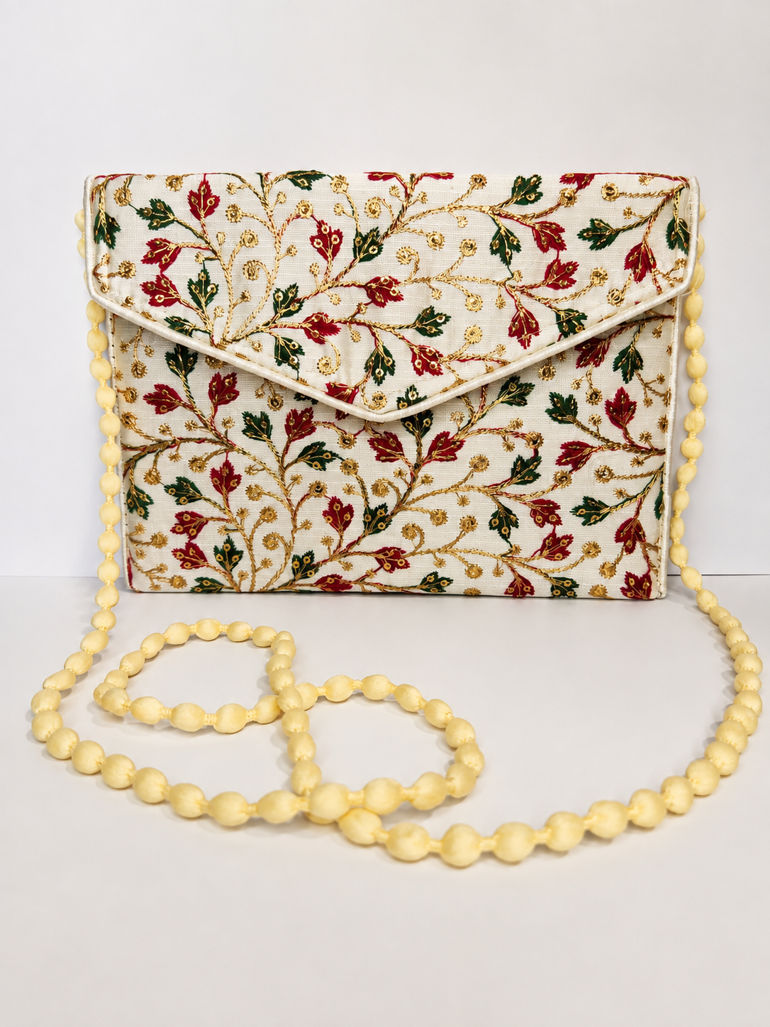 An embroidered cream clutch bag with a floral vine pattern in red, green, and gold, featuring a matching cream beaded shoulder strap.