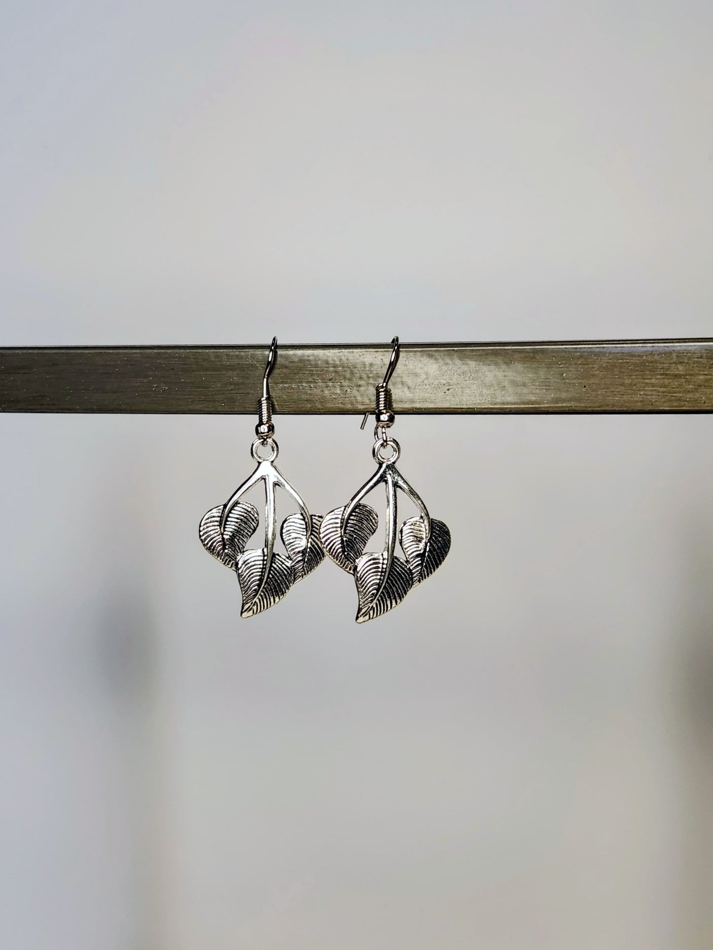 Silver leaf-shaped earrings on a wooden stick against a blurred background