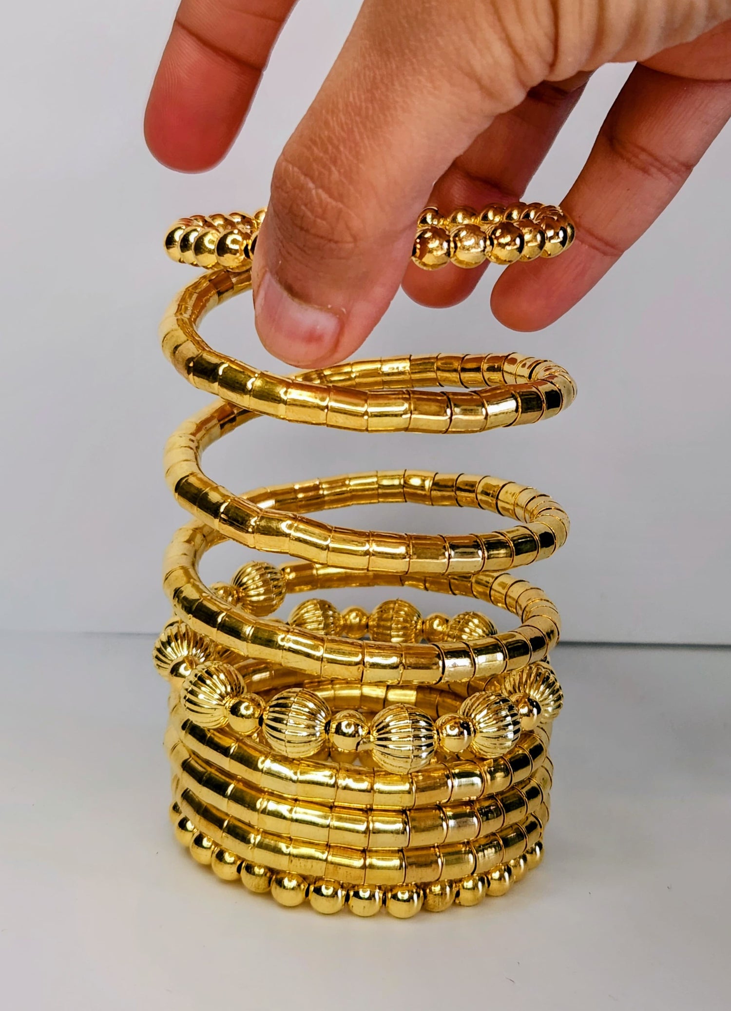 Stack of gold bangles with a hand holding one, on a white background