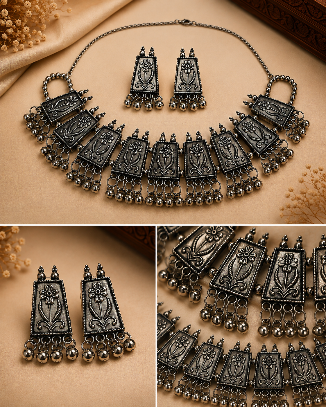A traditional Indian-style jewelry set featuring a statement necklace, matching earrings, and a small pendant, all in an antique silver finish with floral engravings and dangling bell chains. The set is displayed on a beige fabric background with decorative dried flowers.