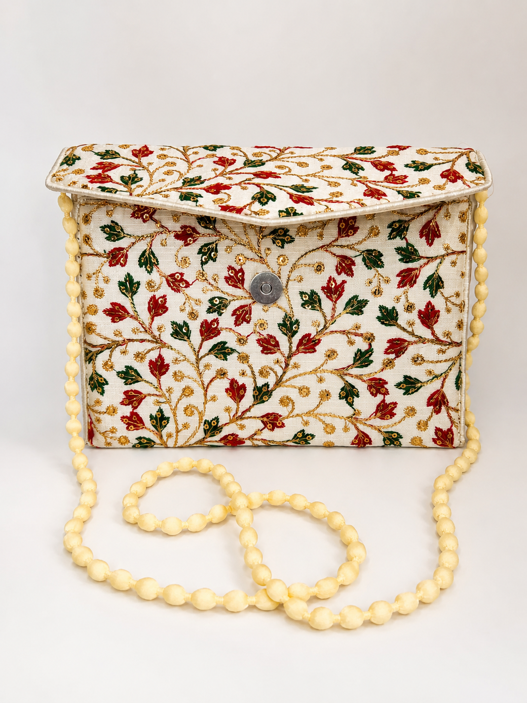 An embroidered clutch bag with a cream base, featuring red and green floral vine embroidery, a silver-tone snap closure, and a thick cream beaded strap, shown on a light gray background.
