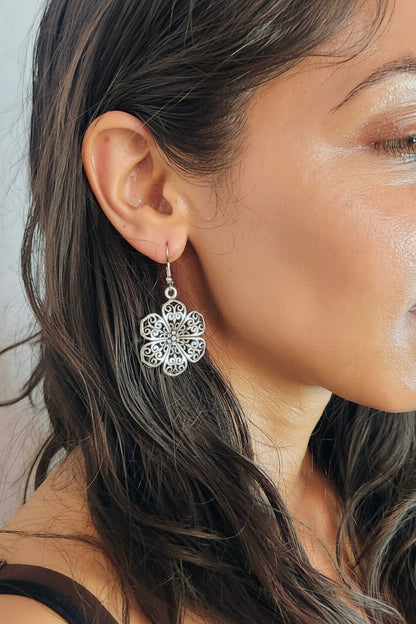 Close-up of a woman wearing a silver floral earring with a neutral background