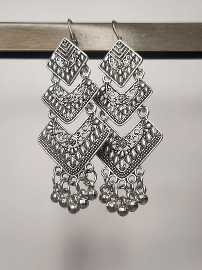 Pair of silver earrings with intricate designs on a reflective surface
