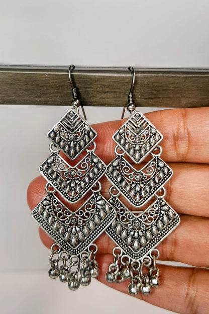 Pair of silver earrings held by a hand against a neutral background