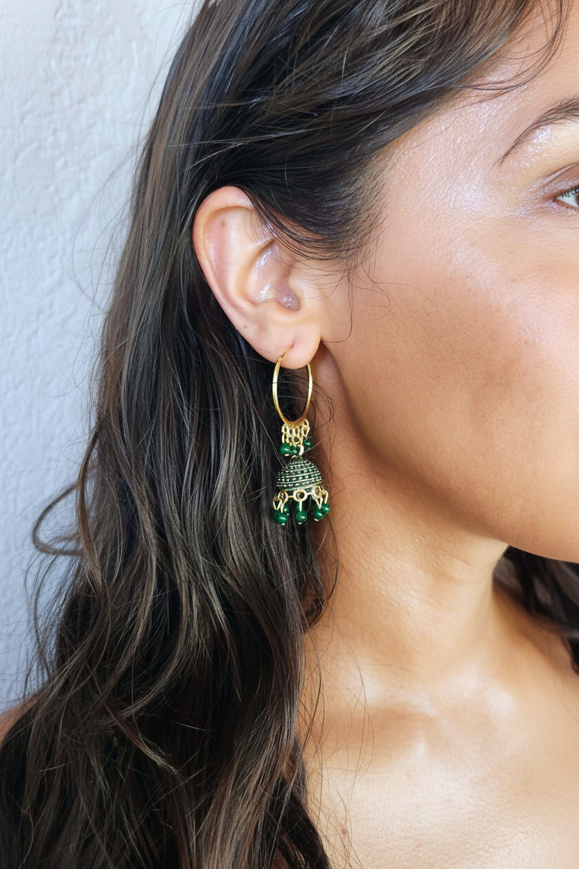 A close-up of a woman's ear wearing a gold hoop earring with a dangling elephant charm decorated with green and gold beads.