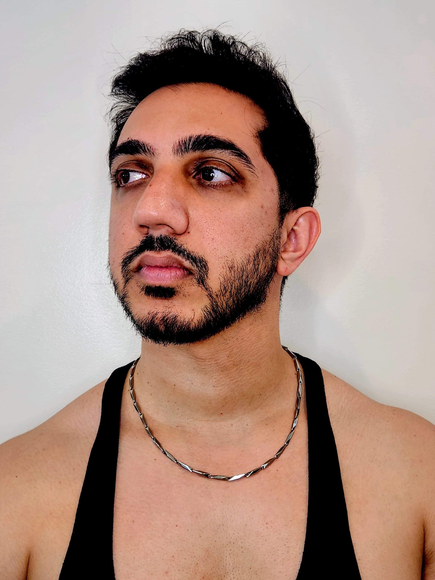 Man wearing a black tank top and silver chain necklace against a plain background