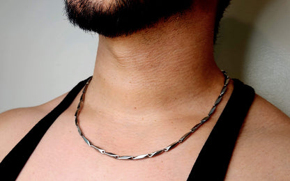 Person wearing a silver chain necklace against a neutral background