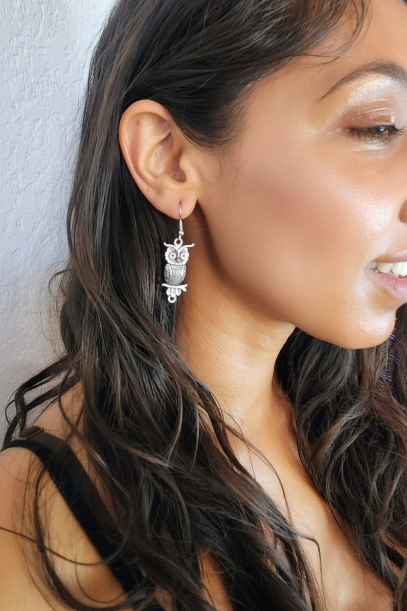 Close-up of a woman wearing owl-shaped earrings with a neutral background
