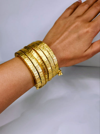 Gold bangles on a wrist against a white background