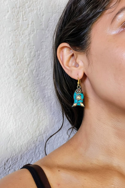 Close-up of a person wearing turquoise earrings with a decorative element against a neutral background