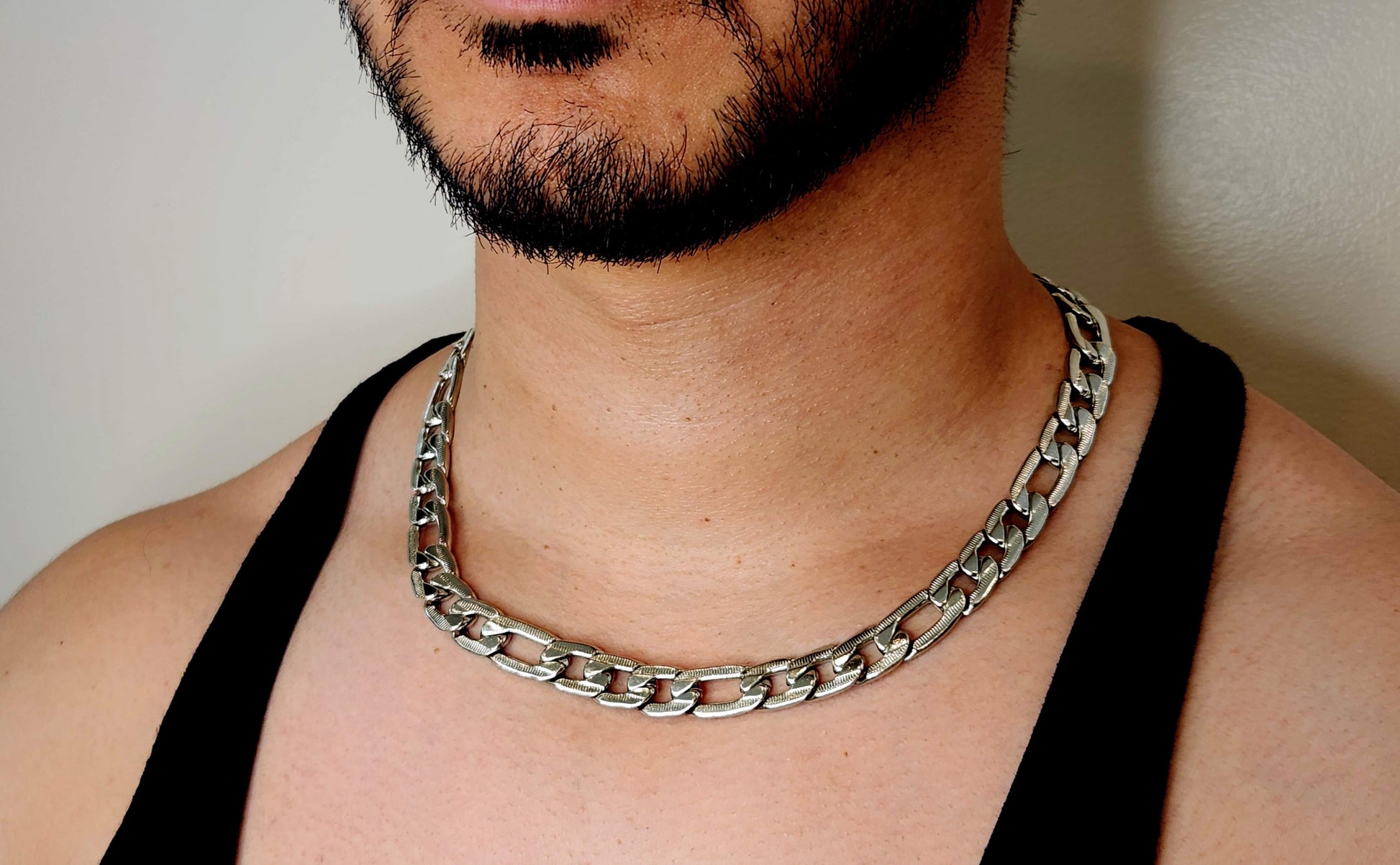 Man wearing a silver chain necklace against a neutral background
